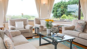 A spacious living room with two sofas, a coffee table, and a view of greenery through large windows. - Bryn Y Mor, Borth Y Gest (Porthmadog)