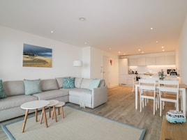 A modern living room with a sectional sofa, a small round table, and a dining area with white chairs.