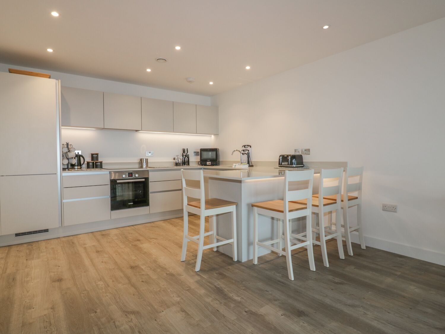 Una cocina moderna con muebles blancos, una isla central con taburetes y electrodomésticos integrados.