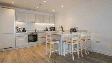 Una cocina moderna con muebles blancos, una isla central con taburetes y electrodomésticos integrados.