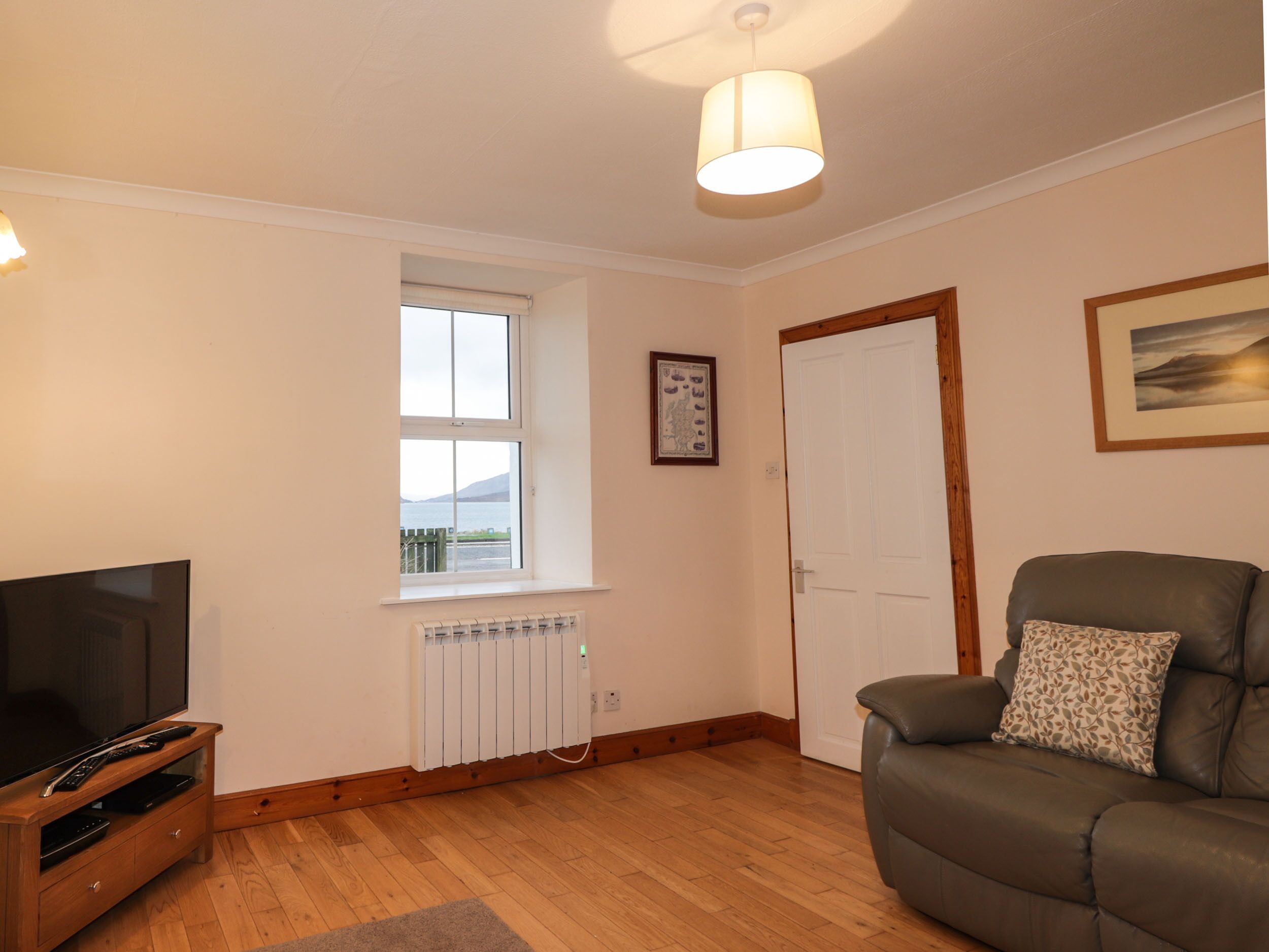 A living room with a flat-screen TV, a sofa, a radiator, and a window with a view.