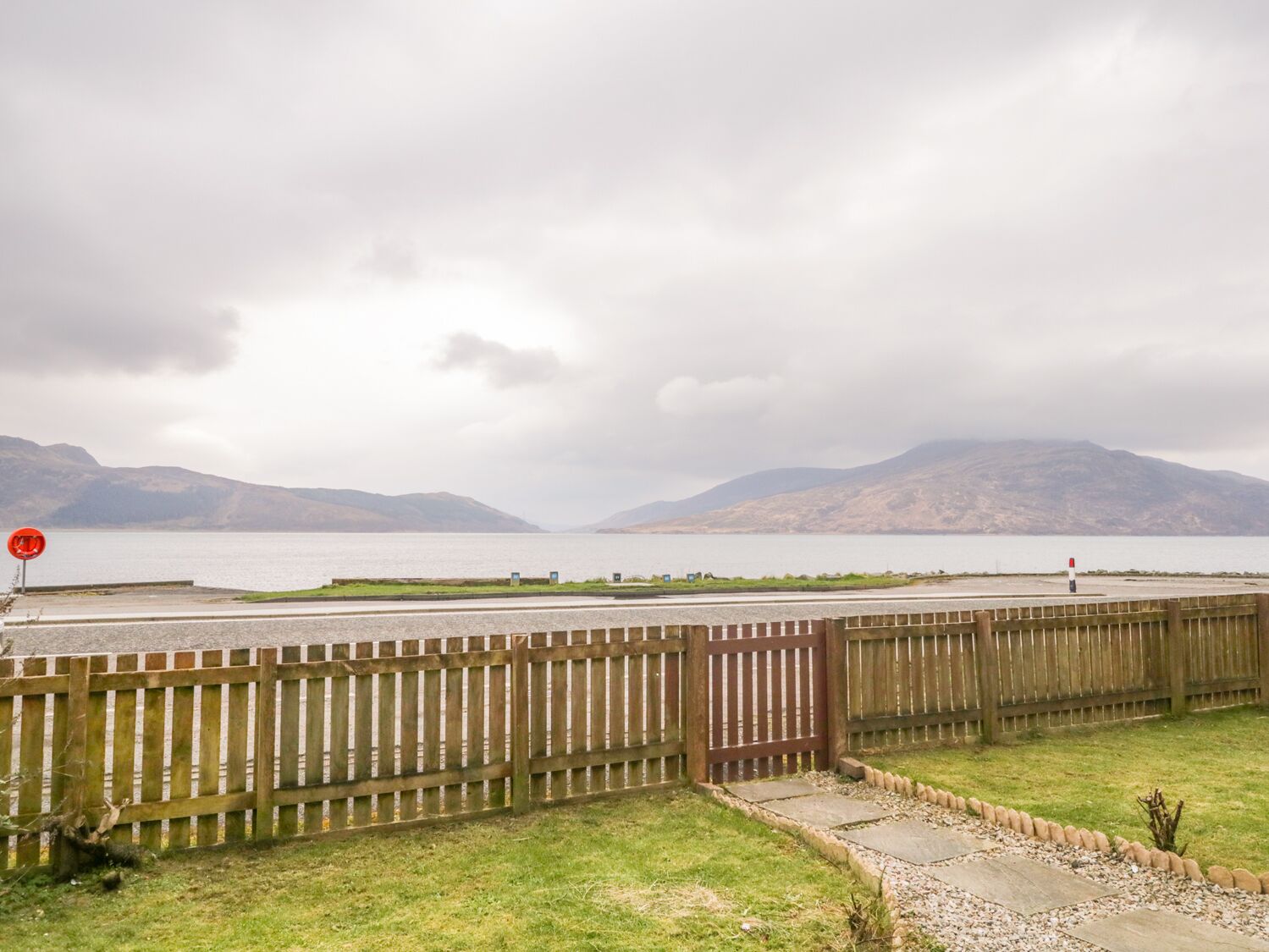 A coastal view with a wooden fence, a clear sky, and distant mountains.