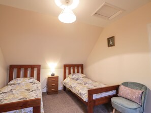 A bedroom with two single beds, a nightstand, a chair, and a ceiling light fixture. - Craigard (Kyle)