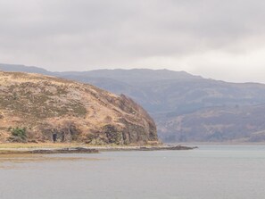 A coastal landscape with a hilly terrain and a calm body of water.