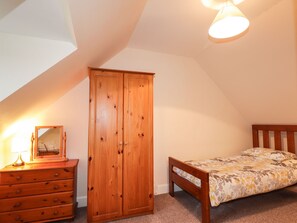A bedroom with a wooden wardrobe, a bed with floral bedding, a nightstand with a lamp, and a ceiling light fixture. - Craigard (Kyle)
