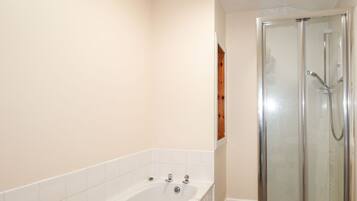 A bathroom with a bathtub, a glass-enclosed shower, and a wooden shelf.