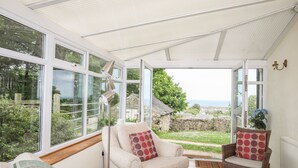 A sunroom with large windows, a comfortable seating area with chairs and cushions, and a view of the surrounding landscape. - Fron Fawr (Pwllheli)