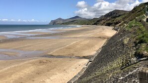 A coastal landscape with a sandy beach, rocky cliffs, and a clear sky. - Fron Fawr (Pwllheli)