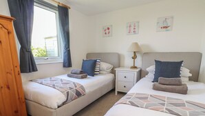 Una habitación de hotel con dos camas, una mesita de noche con lámpara y una ventana con cortinas.