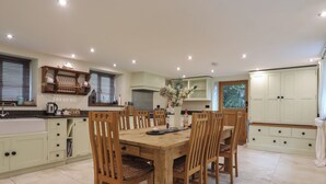 A dining area with a wooden table and chairs, a kitchen with light-colored cabinets, and a window with blinds.