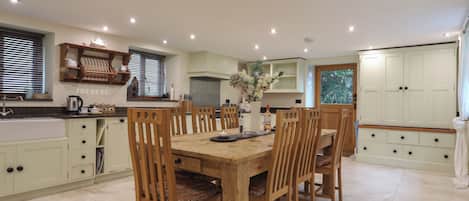 A dining area with a wooden table and chairs, a kitchen with light-colored cabinets, and a window with blinds.