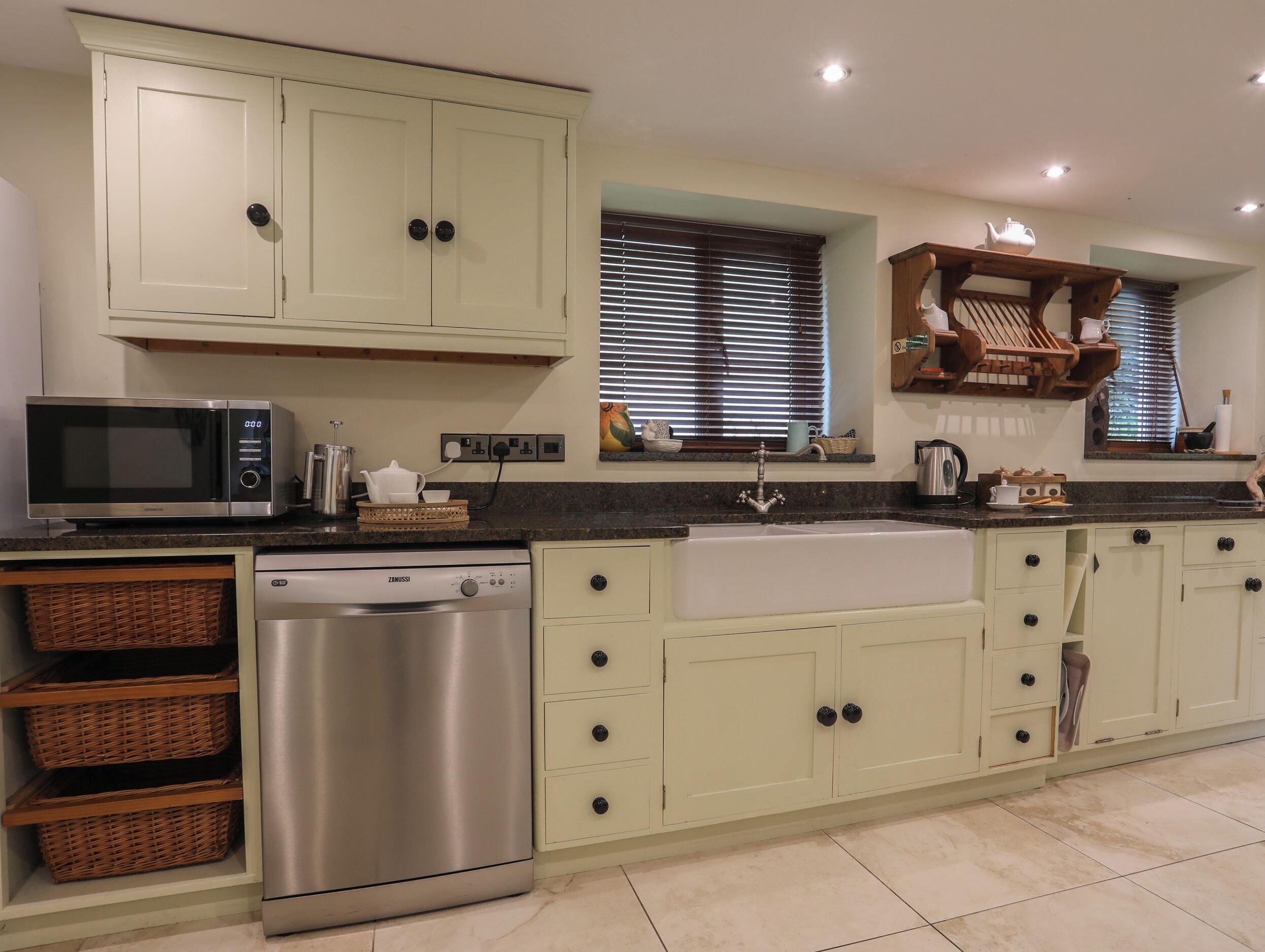 A kitchen with light green cabinets, a stainless steel dishwasher, a microwave, and a sink.