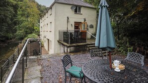 A house with a balcony overlooking a river, surrounded by trees.