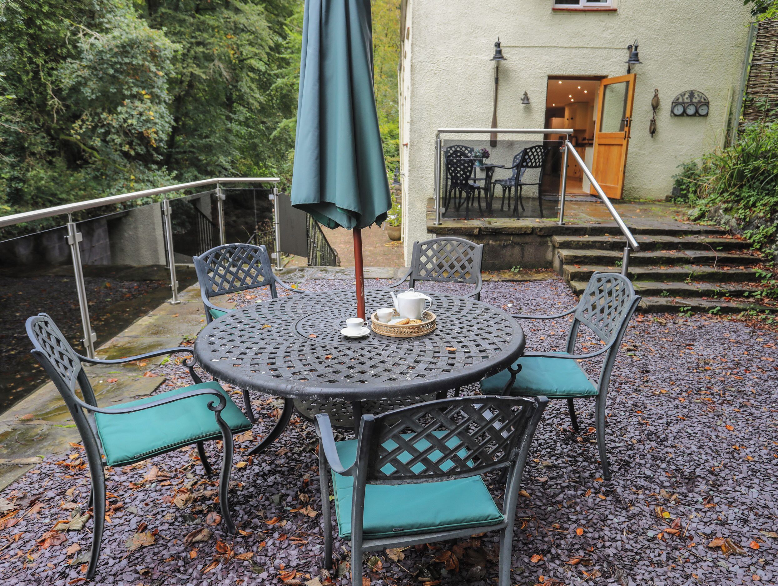 A round metal table with chairs, a table umbrella, and a tray with a cup and cookies.