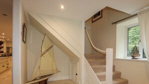 A staircase with a rope handrail, a window with a view of greenery, and a kitchen area in the background.