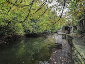 A stone bridge over a calm river, surrounded by dense green foliage. - Melin y Coed (Menai Bridge)
