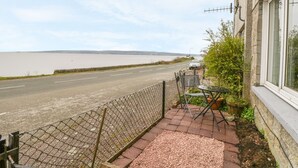 A coastal road with a fence and a table with chairs on a patio. - Pier View (Dunoon)