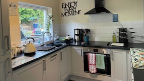 A modern kitchen with white cabinets, a black countertop, a window with a view, and a wall sign that says "ENJOY EVERY MOMENT." - Pier View (Dunoon)