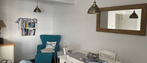 Een gezellige kamer met een blauwgroene fauteuil, een witte eettafel en een boekenkast vol boeken.