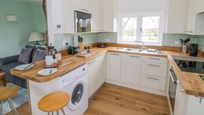 A compact kitchen with a washing machine, a sink, and a window providing natural light. - Wigrams Canalside Cottage (Southam)
