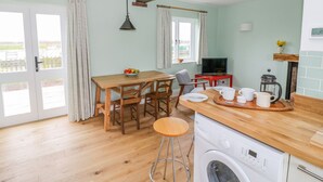 A compact kitchen with a washing machine, wooden dining table, and bar stools. - Wigrams Canalside Cottage (Southam)