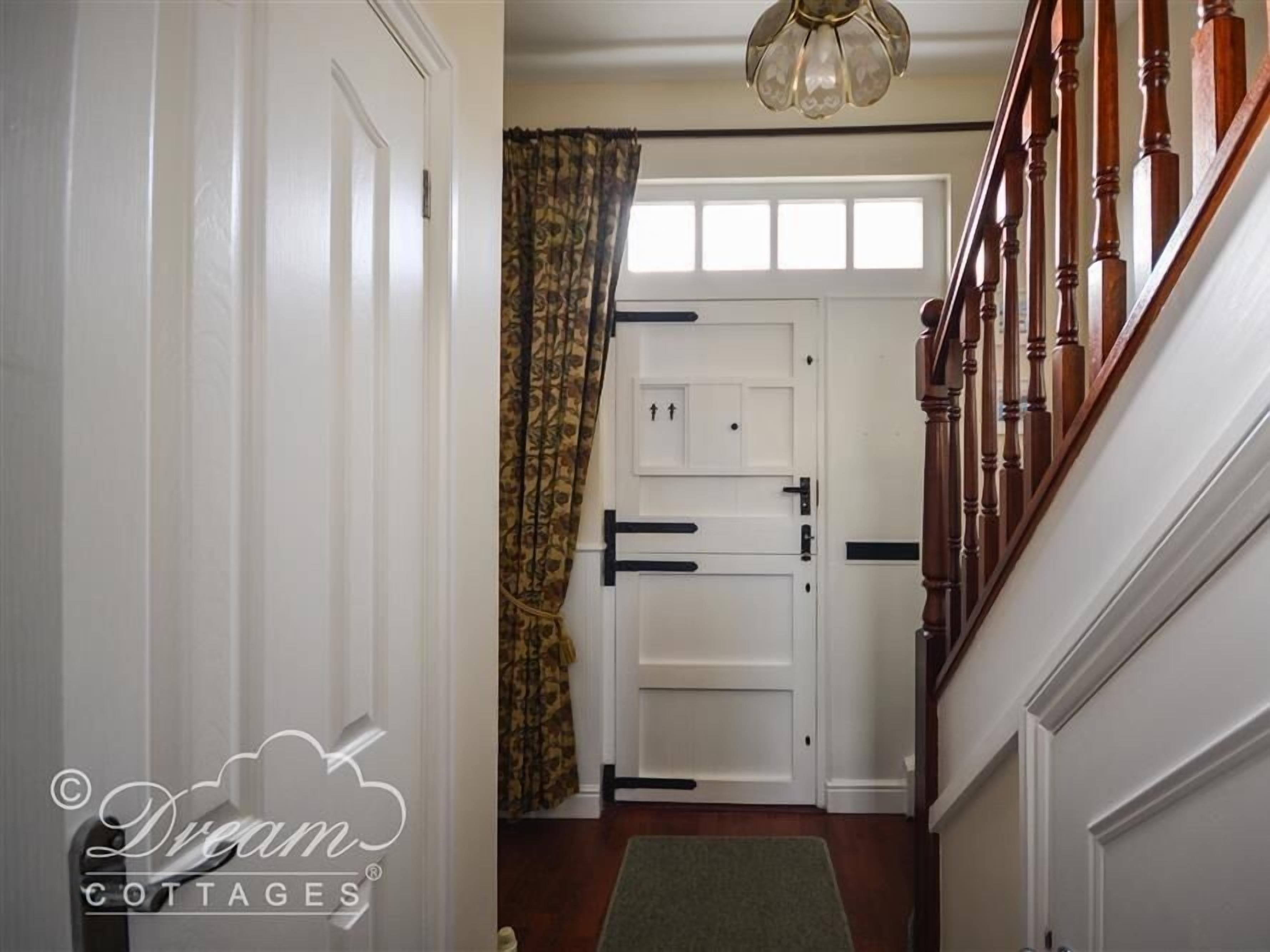 A hallway with a wooden staircase, white doors, and a patterned curtain.