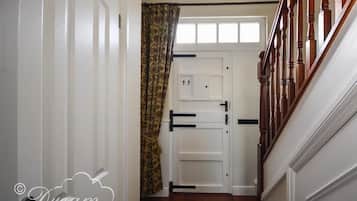 A hallway with a wooden staircase, white doors, and a patterned curtain.