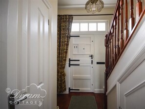 A hallway with a wooden staircase, white doors, and a patterned curtain.