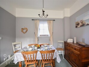 A dining room with a table set for four, a chandelier, a heart-shaped decoration, and a window with curtains.