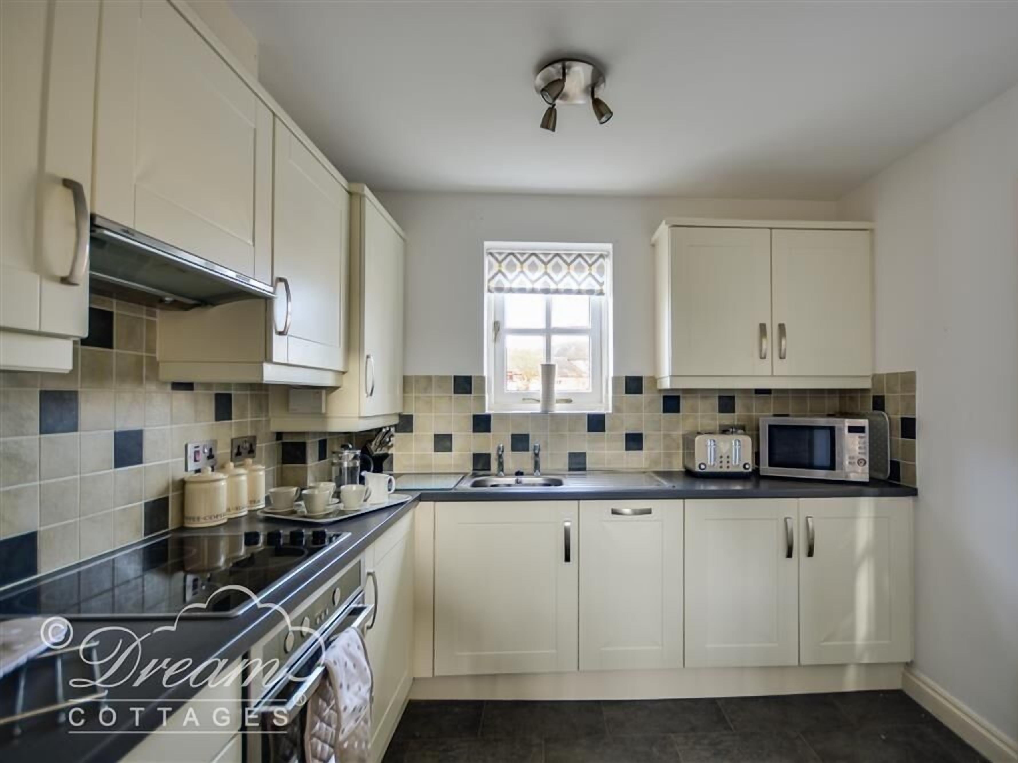 A kitchen with white cabinets, a black countertop, a microwave, a toaster, and a window with patterned curtains.