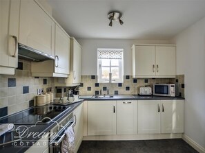 A kitchen with white cabinets, a black countertop, a microwave, a toaster, and a window with patterned curtains.