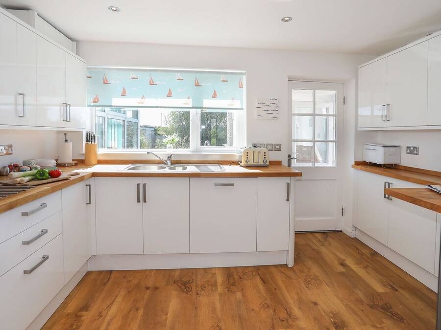 Een moderne keuken met witte kastjes, een houten aanrecht en een raam met afbeeldingen van zeilboten.