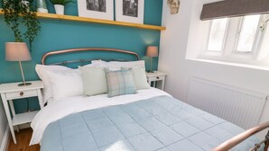 A bedroom with a bed, two bedside tables, a window, and wall-mounted shelves with plants and pictures. - 3 Poole End (Clitheroe)