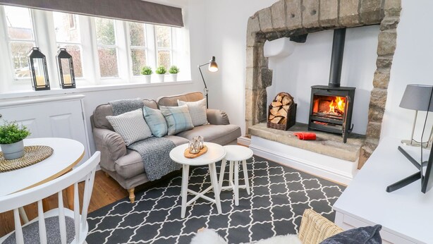 A cozy living room with a stone fireplace, a sofa, a coffee table, and a view of the outside through large windows. - 3 Poole End (Clitheroe)