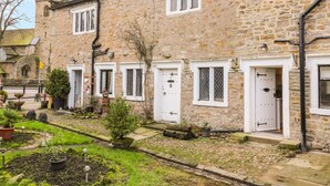 A stone building with multiple white-framed windows and doors, a cobblestone pathway, and a small garden with potted plants. - 3 Poole End (Clitheroe)