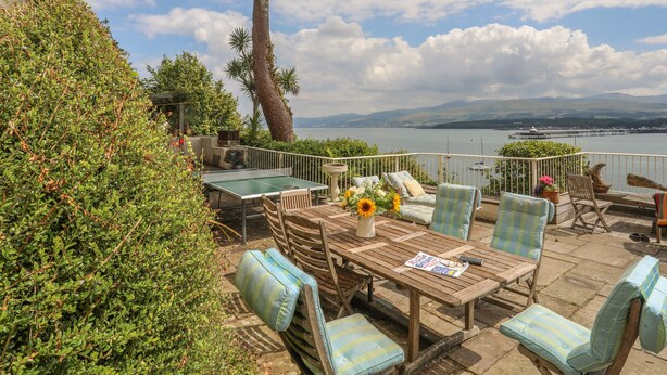 Un patio con mobiliario exterior, una mesa de ping pong y vistas a un lago y montañas.