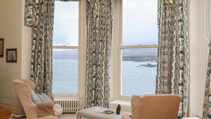 Una habitación con un gran ventanal con vistas a un cuerpo de agua, que incluye dos sillones y una mesita.