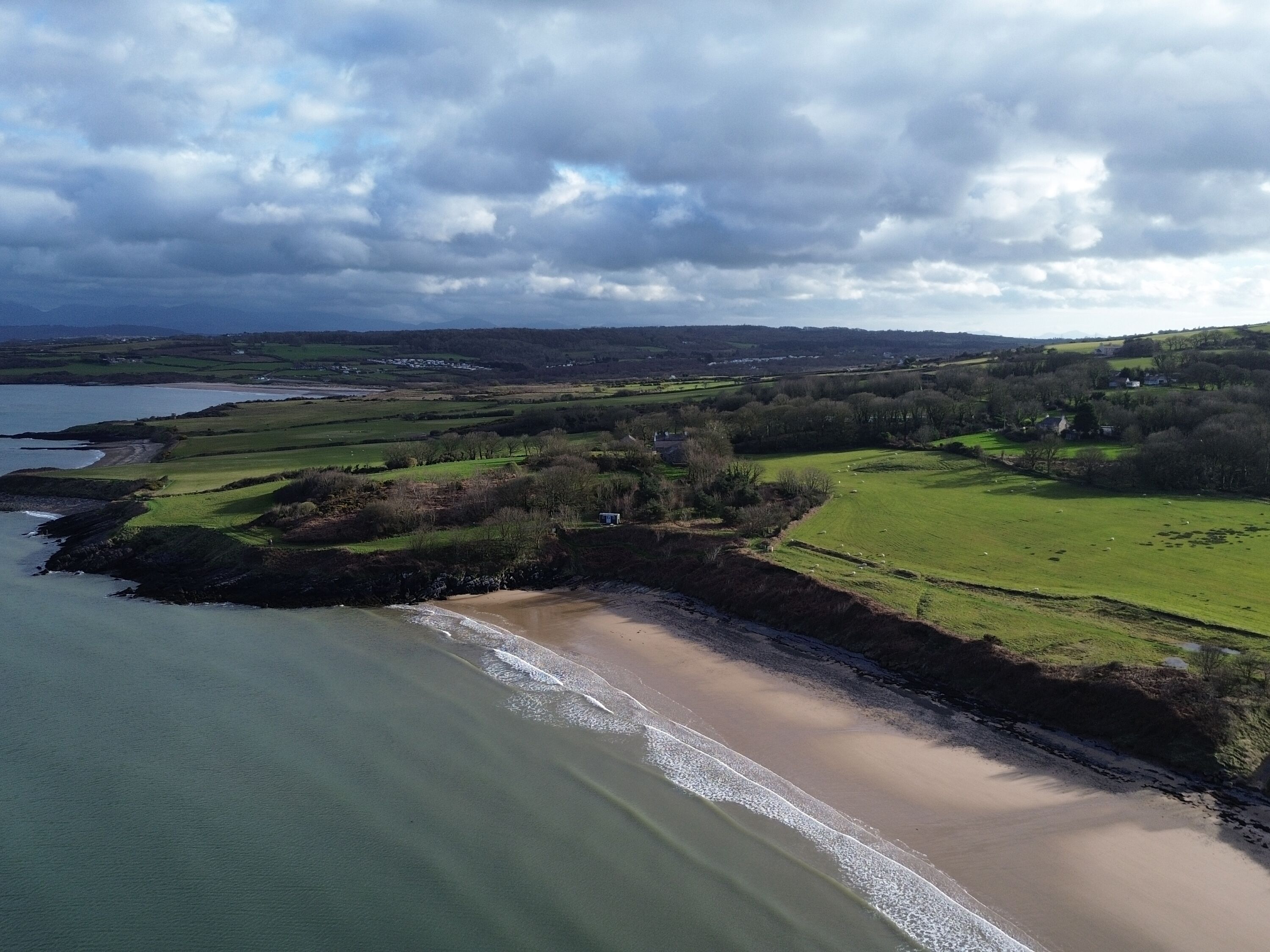 A coastal landscape with a beach, grassy fields, and scattered houses.