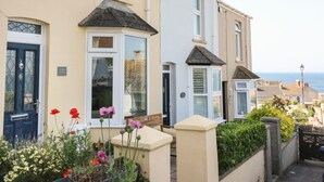 Une rangée de maisons mitoyennes dotées de baies vitrées, un jardin fleuri et une vue sur la mer.