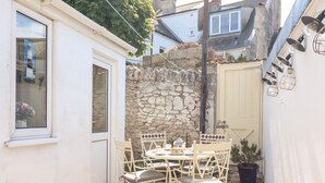 Une petite terrasse avec une table ronde et quatre chaises, un mur en pierre et une porte blanche.