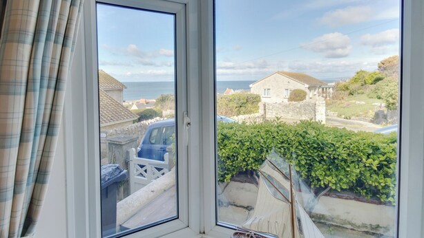 Une vue depuis une fenêtre donnant sur une zone côtière, avec une maison en pierre, de la verdure et une voiture garée.