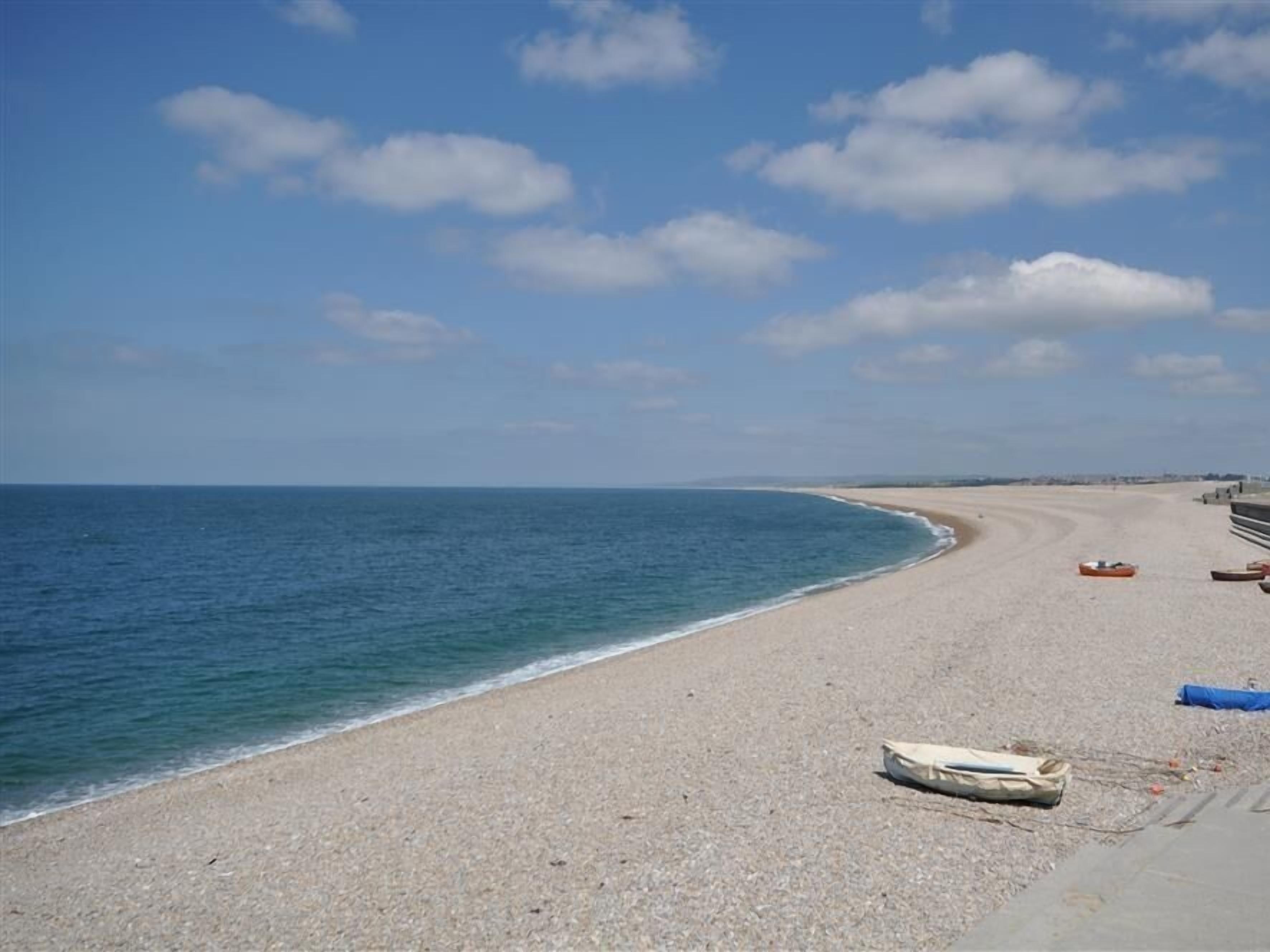 A beach with a clear sky, calm sea, and a few boats on the shore.