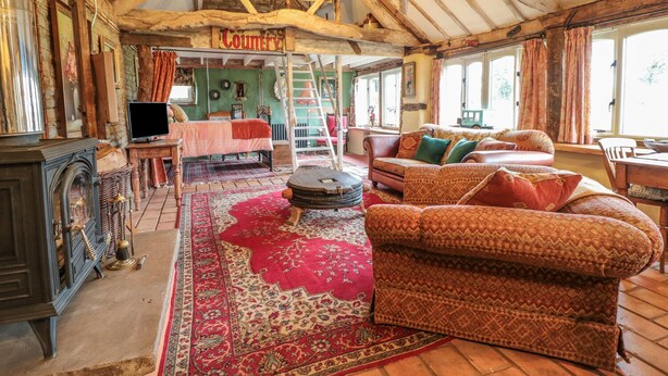 A rustic interior with exposed wooden beams, a large red patterned rug, a sofa, and a bed with a green wall in the background. - Jackdaw's Roost (Gloucester)