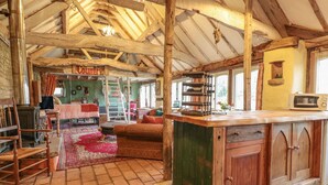 A rustic interior with exposed wooden beams, a central island with a sink, a dining area with a red tablecloth, and a sign that reads "Country". - Jackdaw's Roost (Gloucester)