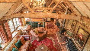 A rustic interior with exposed wooden beams, a chandelier, a sofa set, a fireplace, and a dining area. - Jackdaw's Roost (Gloucester)