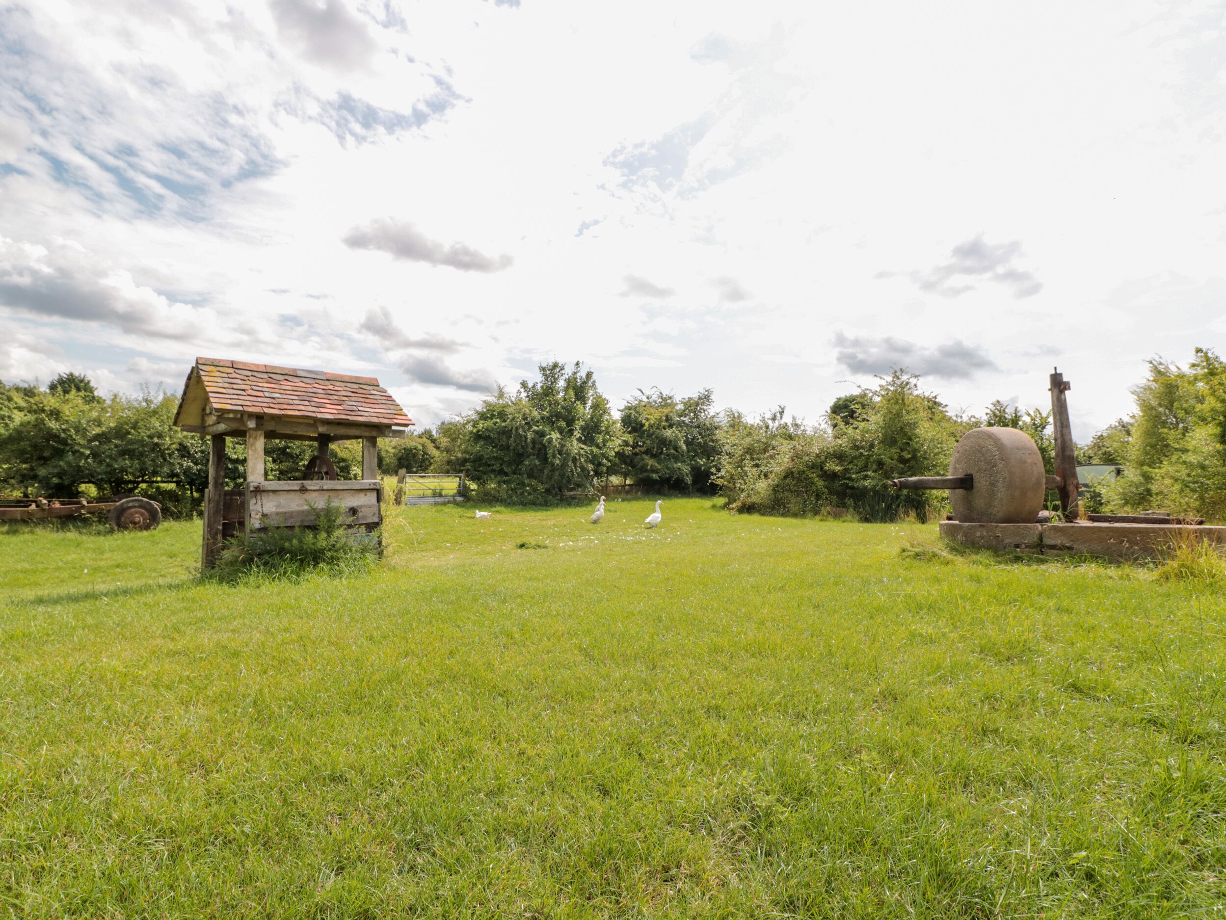 A rustic outdoor setting with a small wooden structure, possibly a gazebo, and a large stone mill.
