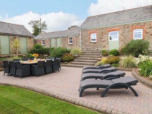 A courtyard with a dining area, lounge chairs, and a stone building with steps leading to a door. - Silvermine House (St Austell)