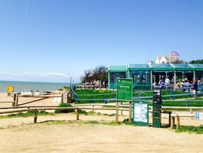 A beachside cafe with outdoor seating, a flag, and a signboard.