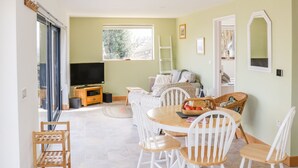 Ein gemütliches Wohnzimmer mit Fernseher, einer Couch, einem Esstisch mit Stühlen und einem Fenster mit Blick auf Bäume.