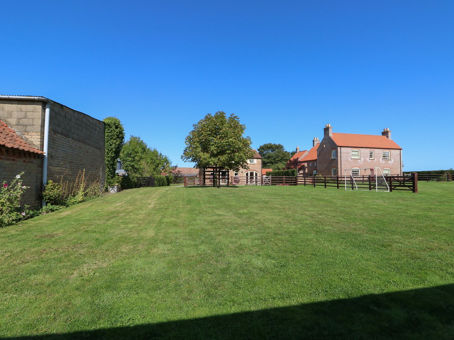 A large, open grassy area with a brick building and a wooden fence in the background.